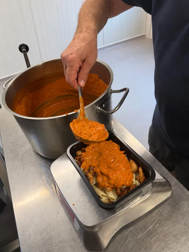 Huisgemaakte saus wordt over penne met kip geschept