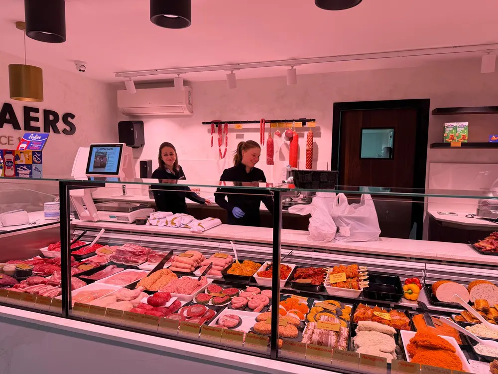 Twee medewerkers achter de toog met vers vlees, worsten en gemarineerde spiesen