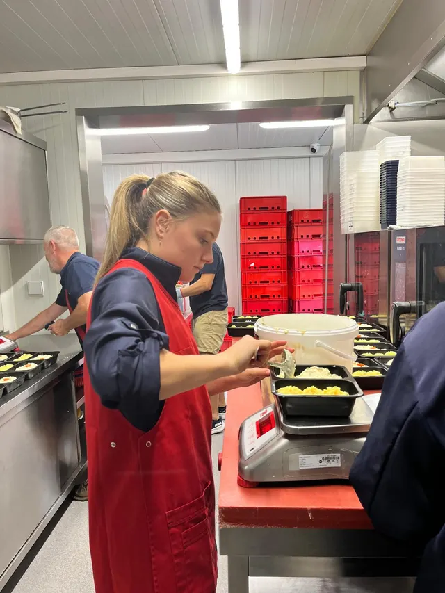 Medewerkers vullen in het atelier bakjes met puree en saus voor de traiteurtoog